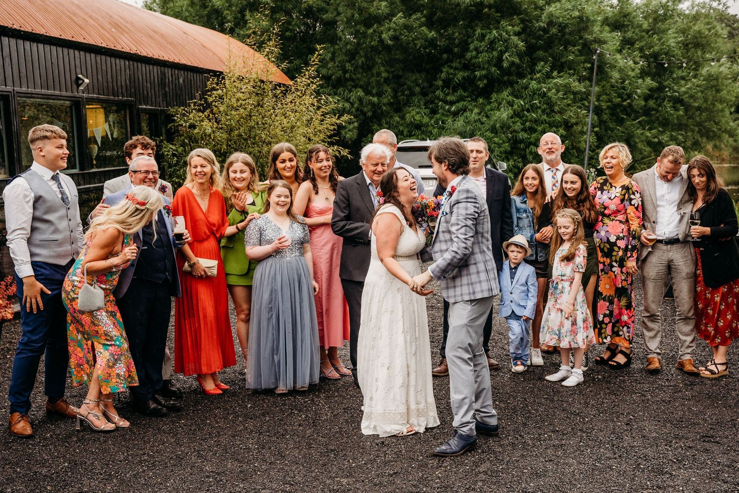 Wedding party celebrates with newlyweds outside rustic venue with tin roof on a sunny summer day. Wedding photographer Dublin