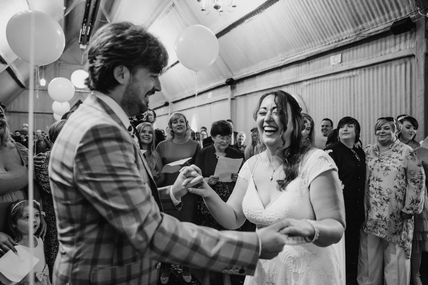Wedding guests dancing and celebrating in a rustic venue with white balloons and bunting decorations. Wedding photographer Dublin