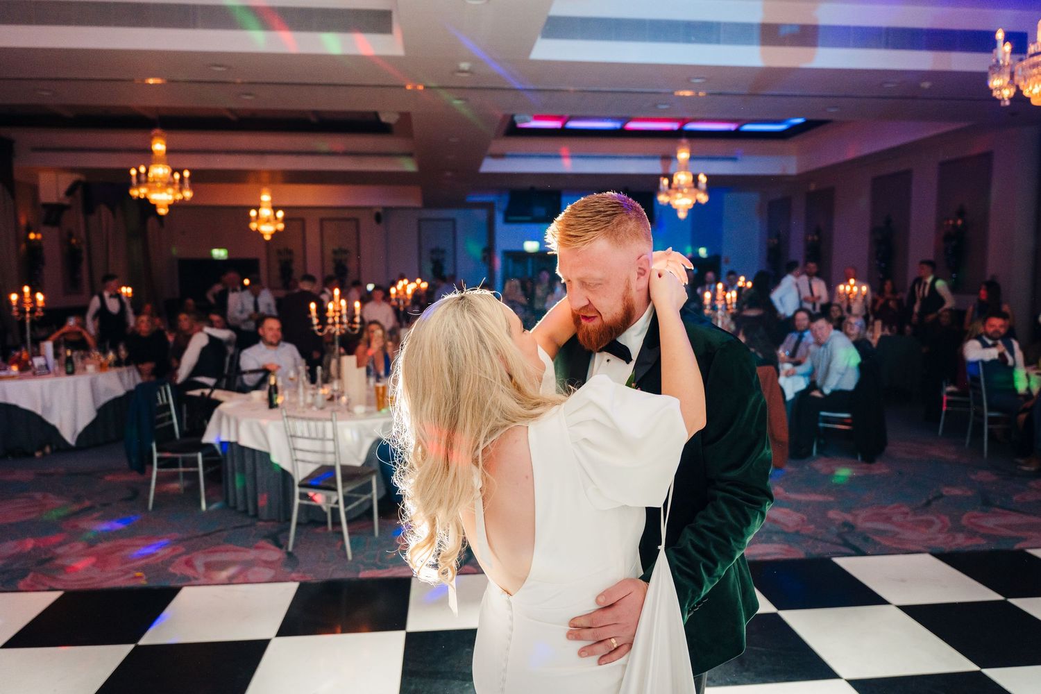 Newlyweds dance together in a reception hall with colorful lighting and checkerboard floor. City Hall Dublin Photographer