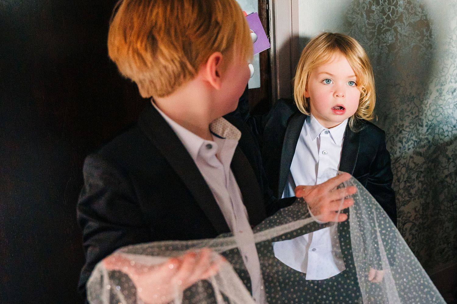 Two children in formal attire stand together against a dark background, one gesturing while the other listens. City Hall Dublin Photographer