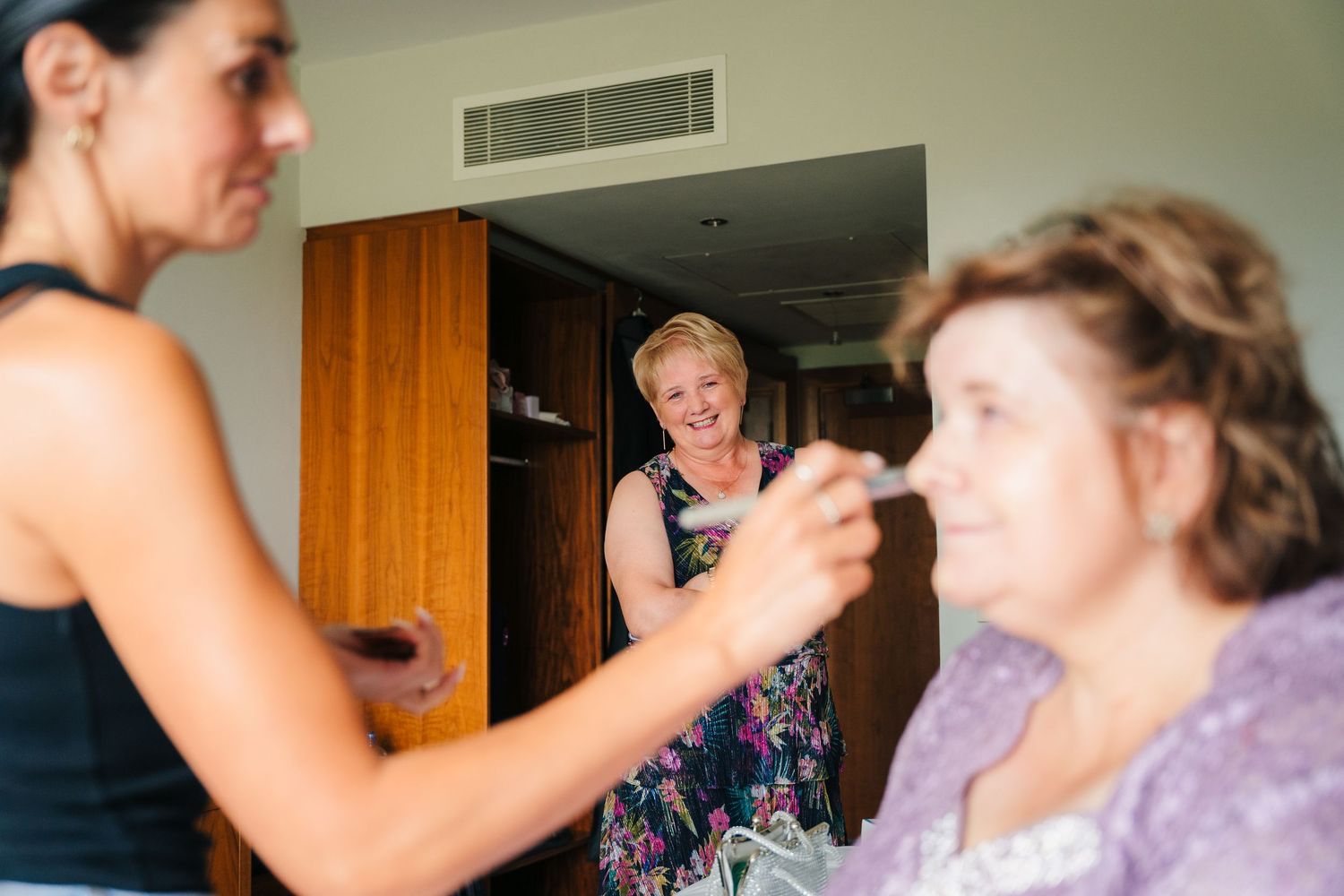 Makeup artist works with focus and precision during bridal preparation session in warm-lit room. Portmarnock Hotel Wedding PHOTOGRAPHER Dubl