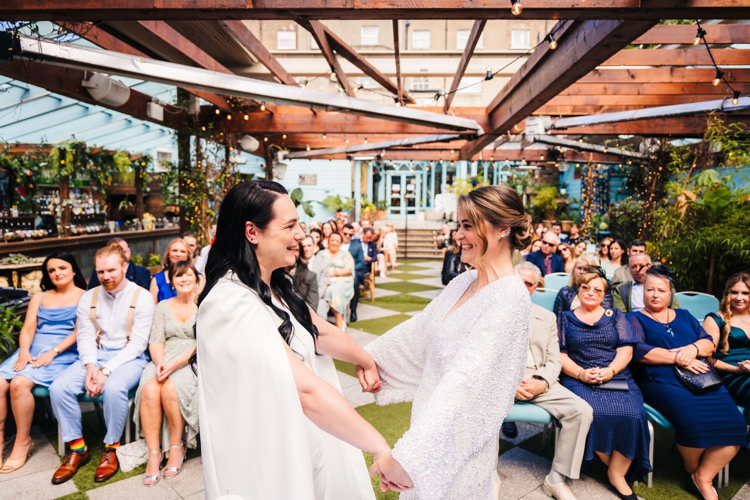 A joyous outdoor wedding celebration under a wooden pergola with guests seated in rows. House Dublin Wedding Photographer