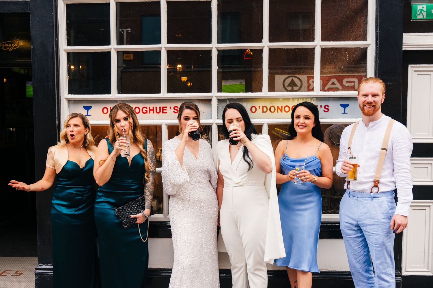 A wedding party poses outside a storefront wearing elegant dresses in teal and white. House Dublin Wedding Photographer