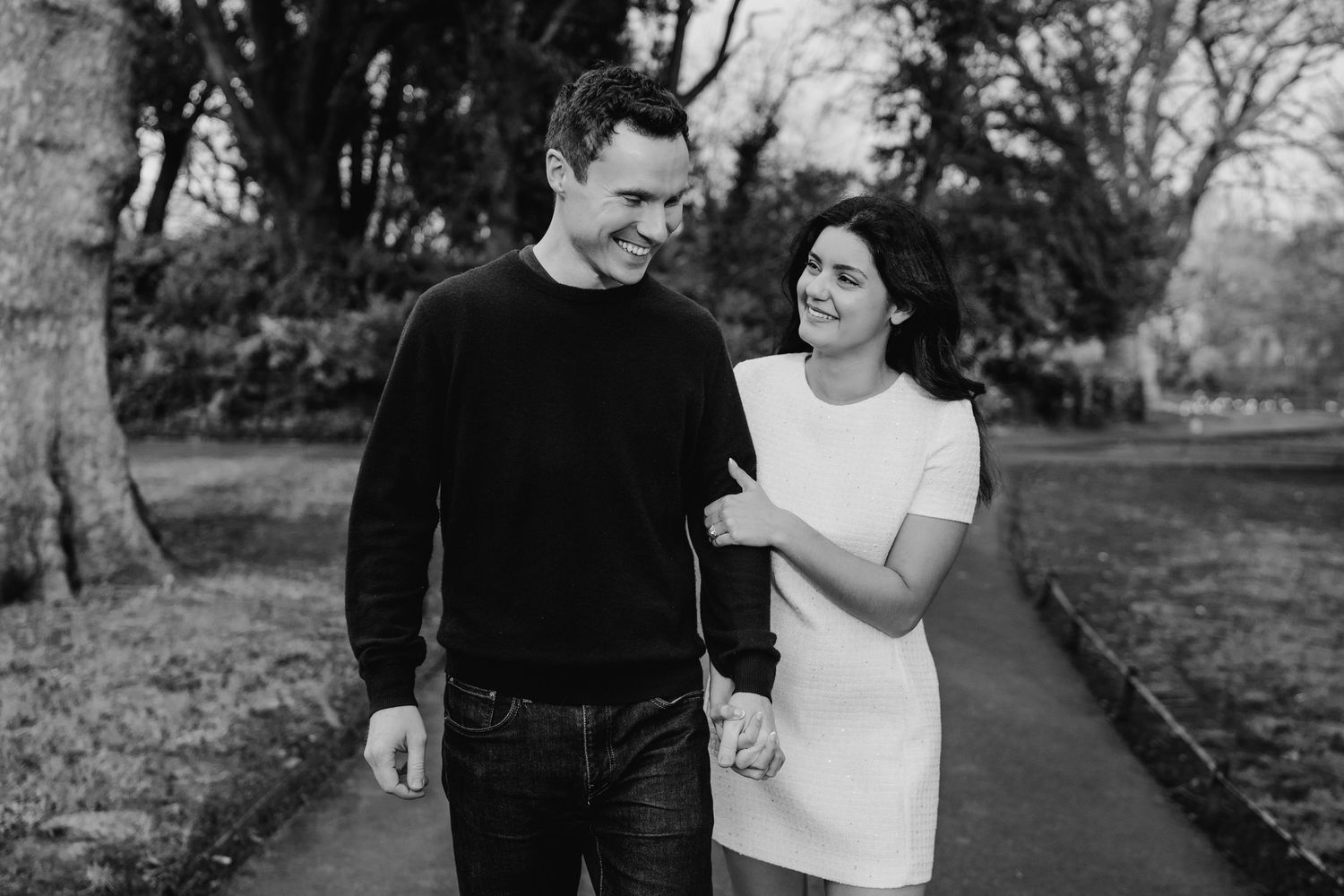 A couple in casual black and white attire shares joyful moments while walking together outdoors in a natural setting. Surprise proposal dubl
