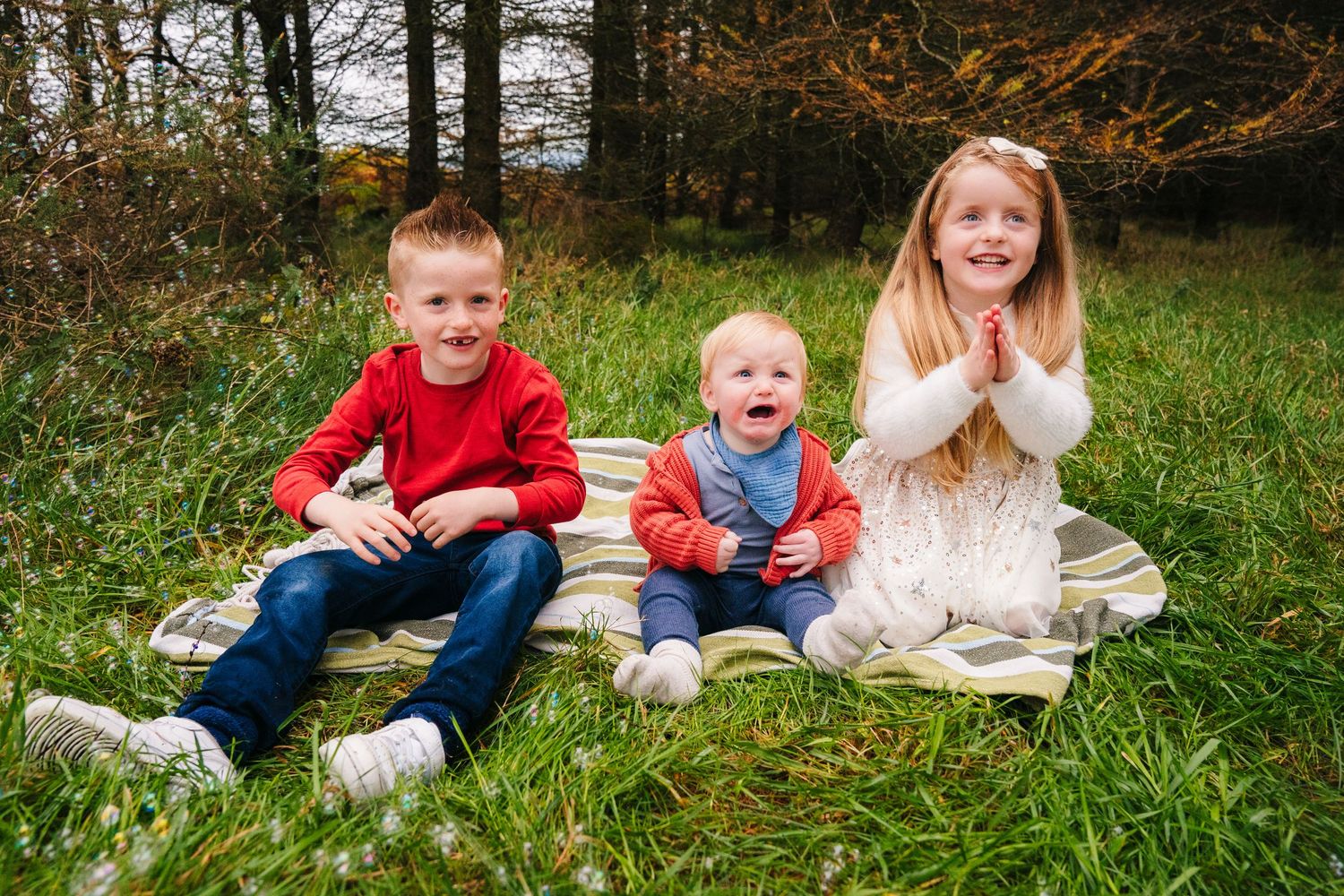 Family relaxing together on blanket in grassy field during fall photoshoot.