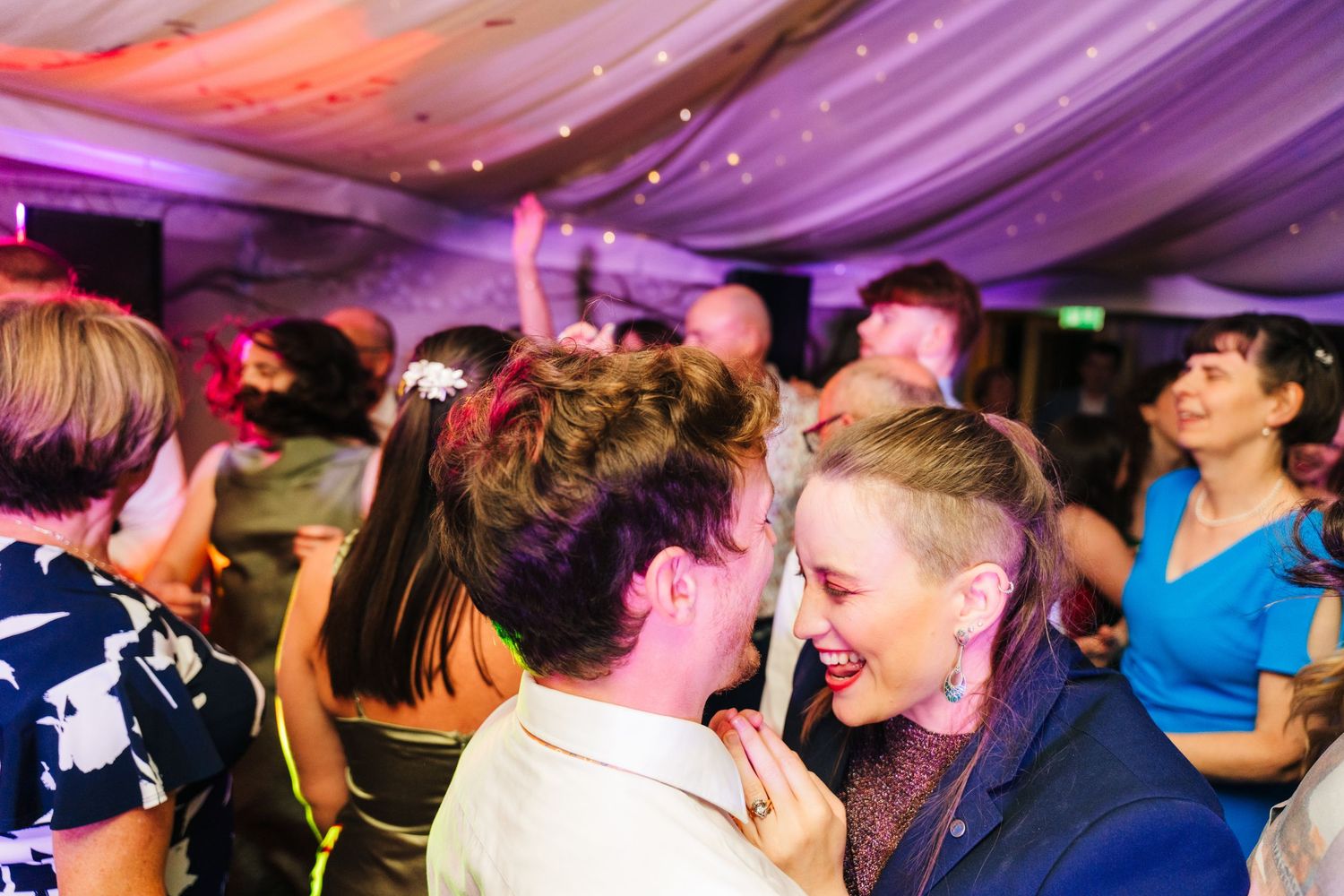 Millhouse slane wedding photogWedding guests dancing and celebrating under purple and pink illuminated tent draping at an evening reception.
