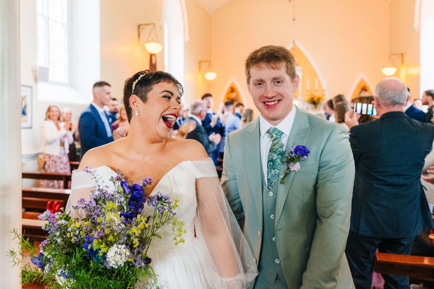 Millhouse slane wedding photographerWedding guests celebrate at an elegant indoor reception venue with floral decorations and soft lighting.