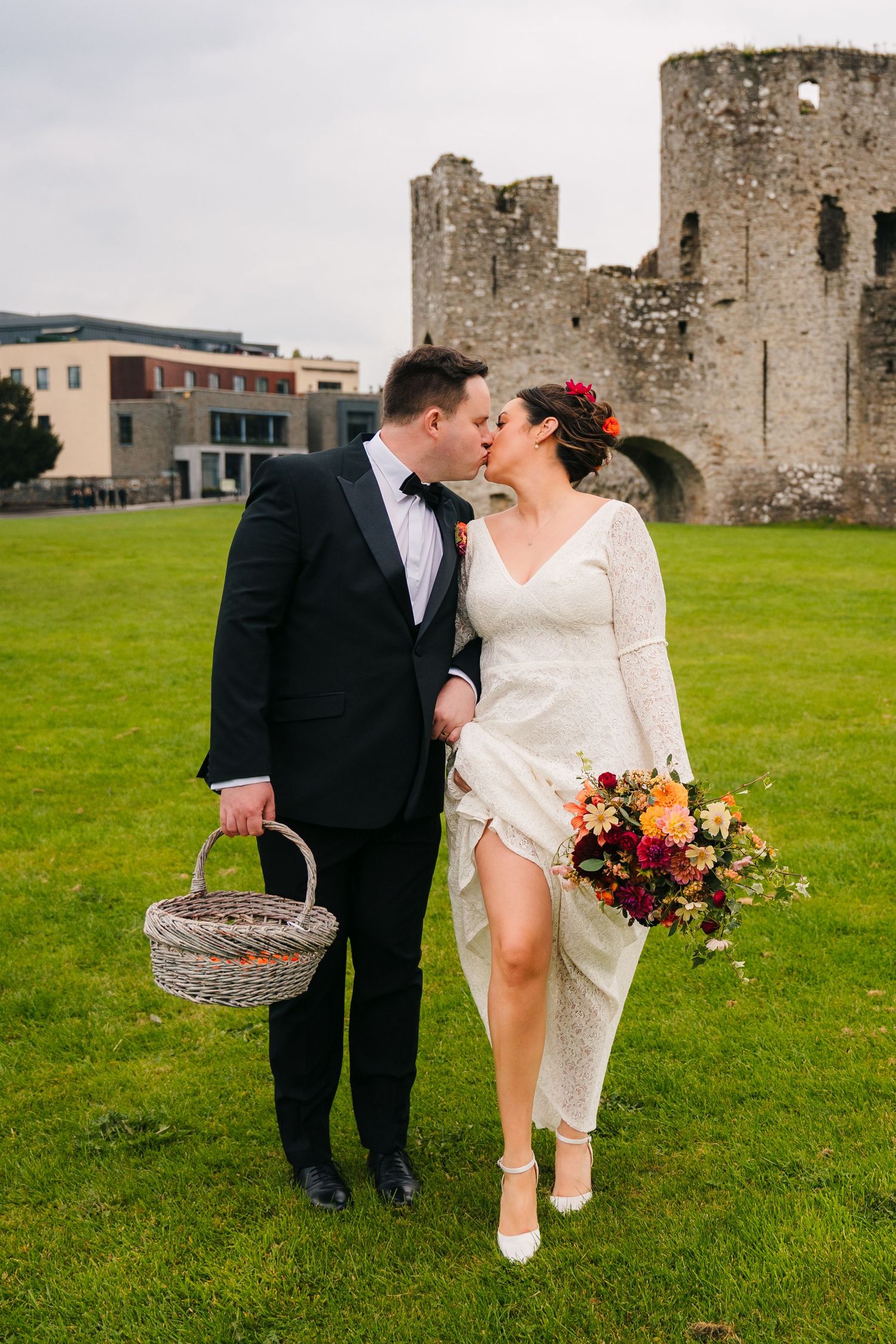 A romantic wedding portrait of a couple sharing a kiss in front of ancient castle ruins on a green lawn. Wedding Photography Trim Castle Ire