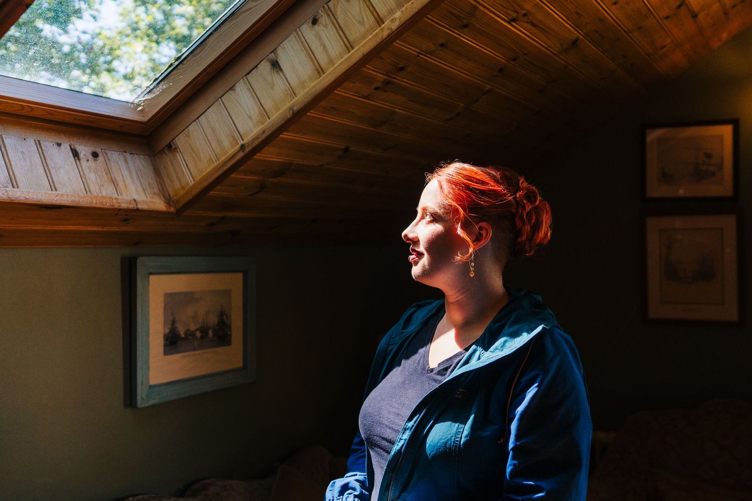 Poulaphouca Wedding photograpPerson sitting by a window in a rustic cabin interior, looking up and smiling with natural light streaming in.
