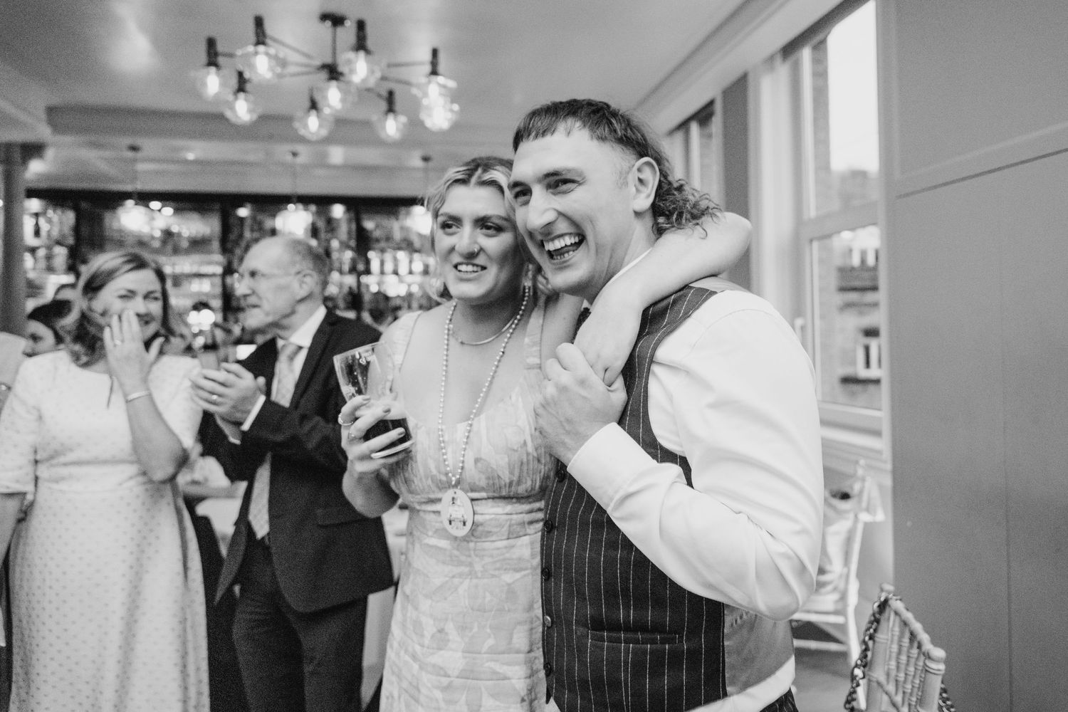 Wedding guests share a candid laughing moment during a black and white reception photo. PHOTOGRAPHER Dublin Ireland Wedding