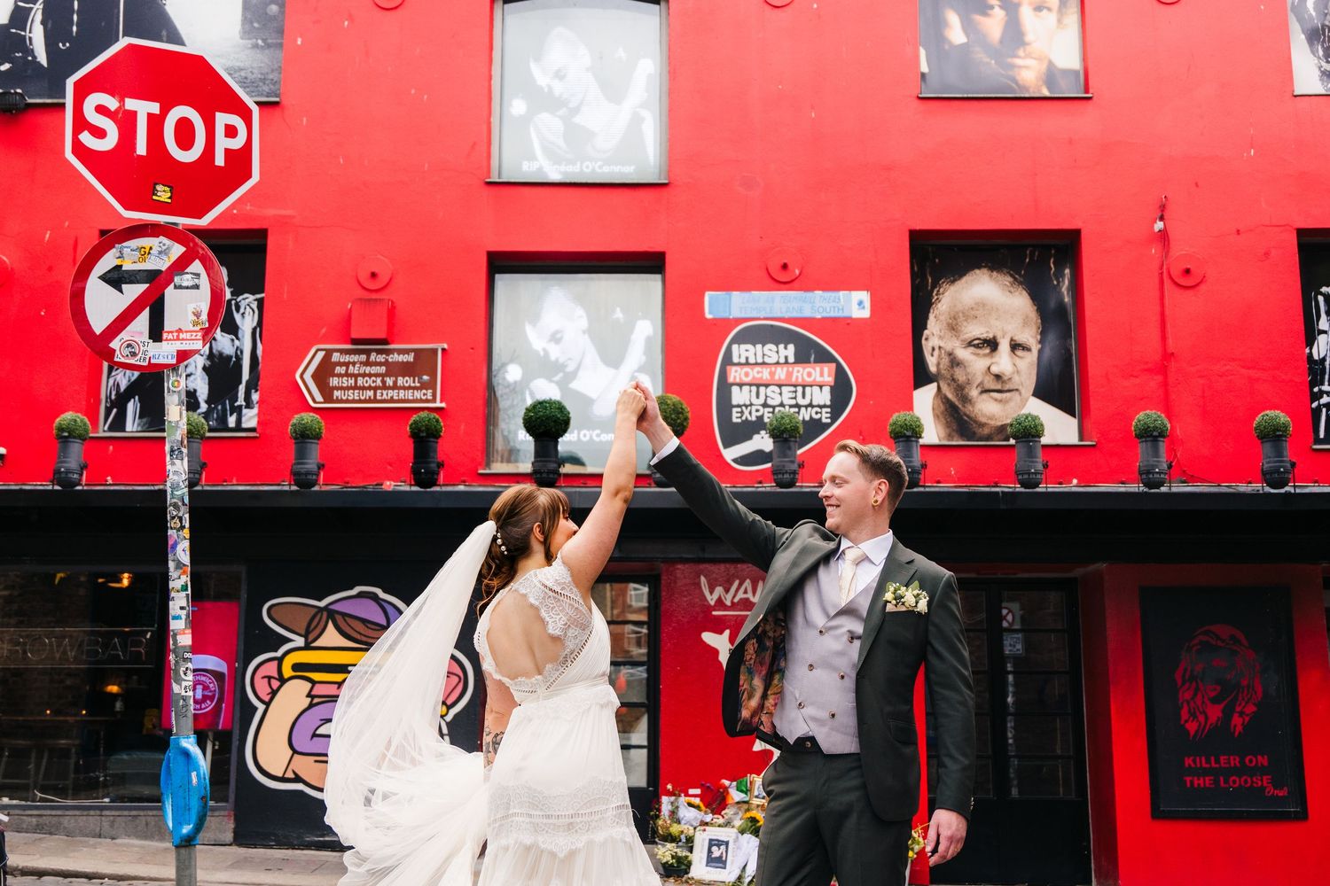 A playful wedding photo in front of a vibrant red building with street signs. PHOTOGRAPHER Dublin Ireland Wedding