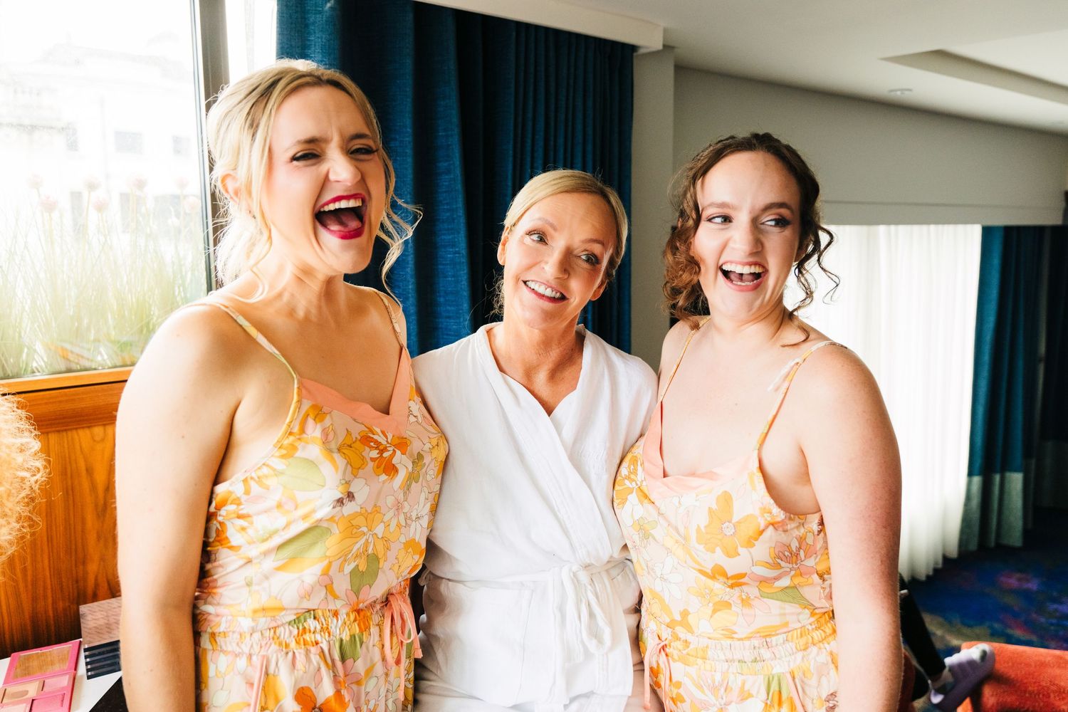 Three people in matching floral dresses sharing joyful laughter in a cruise ship cabin. PHOTOGRAPHER Dublin Ireland Wedding