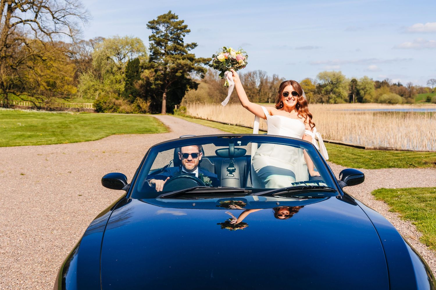 Castle Leslie Wedding Photographer Dublin A celebration in a blue convertible car parked in a scenic spring landscape.
