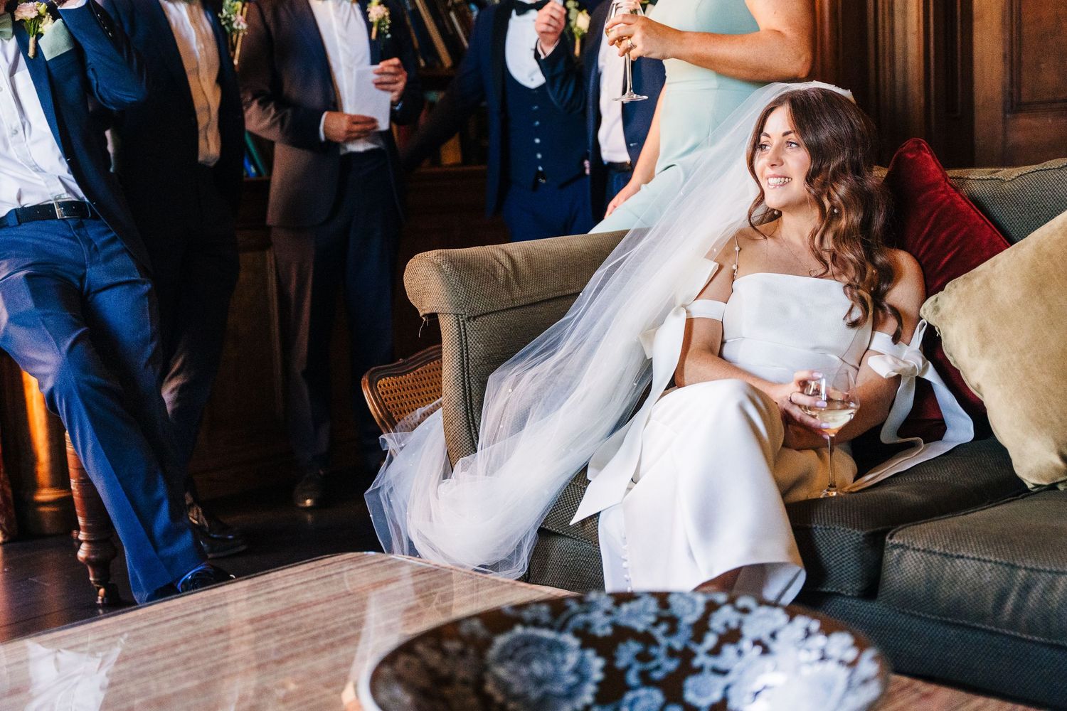 Castle Leslie Wedding Photographer Dublin A bride in a white off-shoulder dress relaxes on a leather couch during her wedding reception.