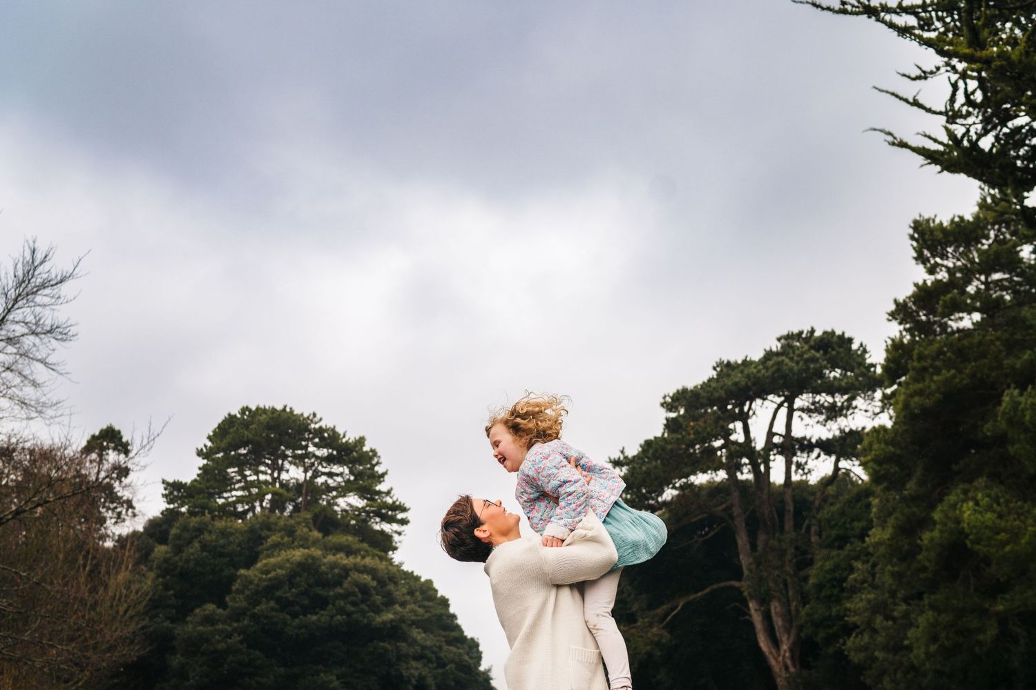 Family photographer Dublin Ireland  A tender moment of play and connection in a park with tall trees.