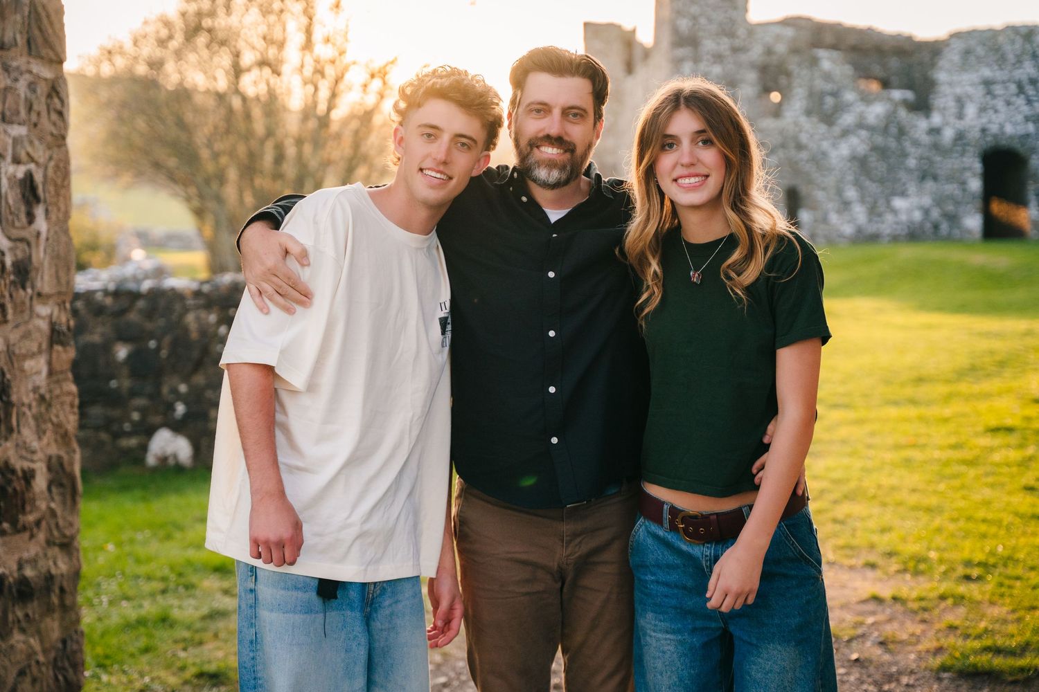 Three friends posing together near historic stone ruins during golden hour. Photographer Ireland dublin