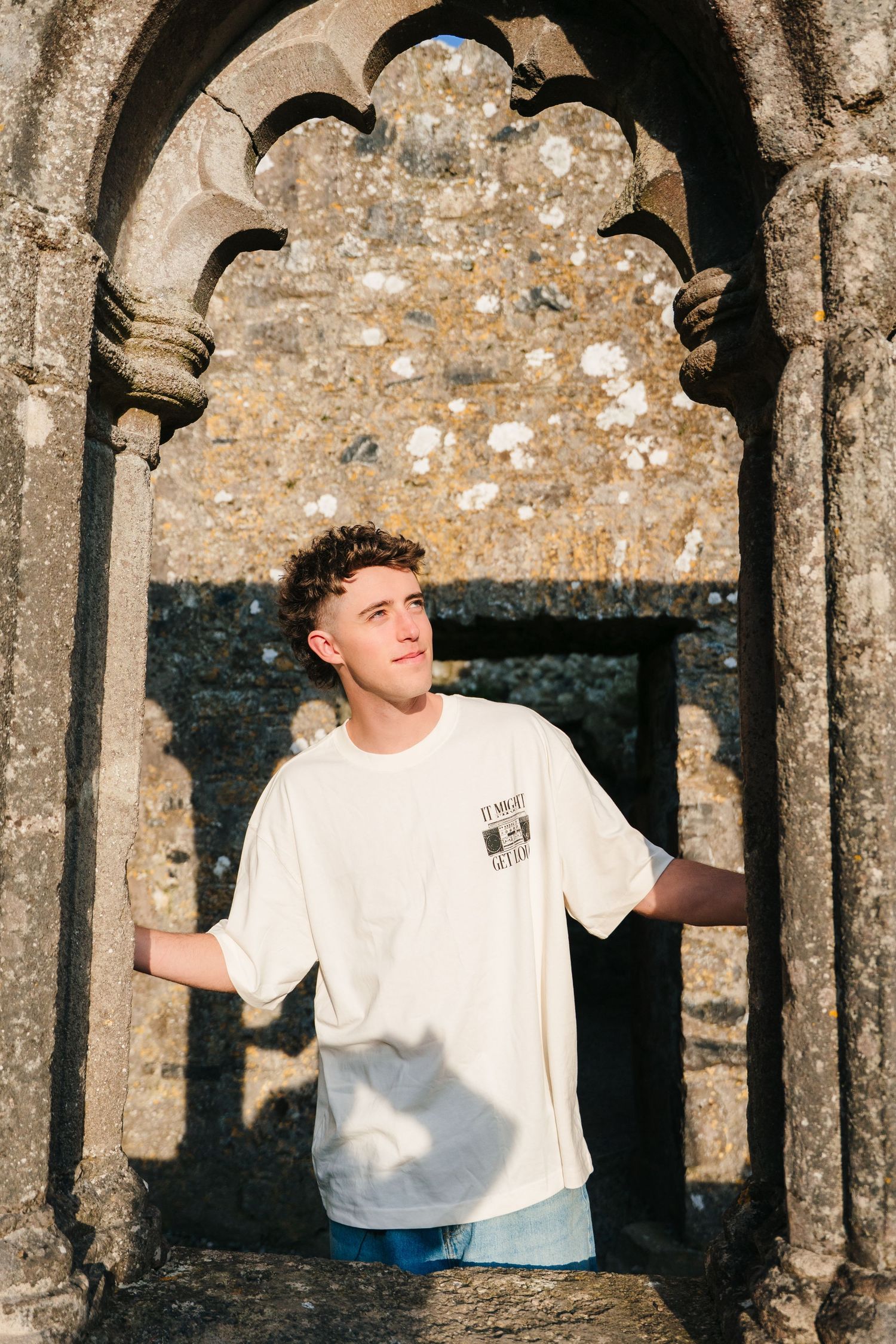 A person in a white t-shirt poses playfully in a gothic stone archway. Photographer Ireland dublin
