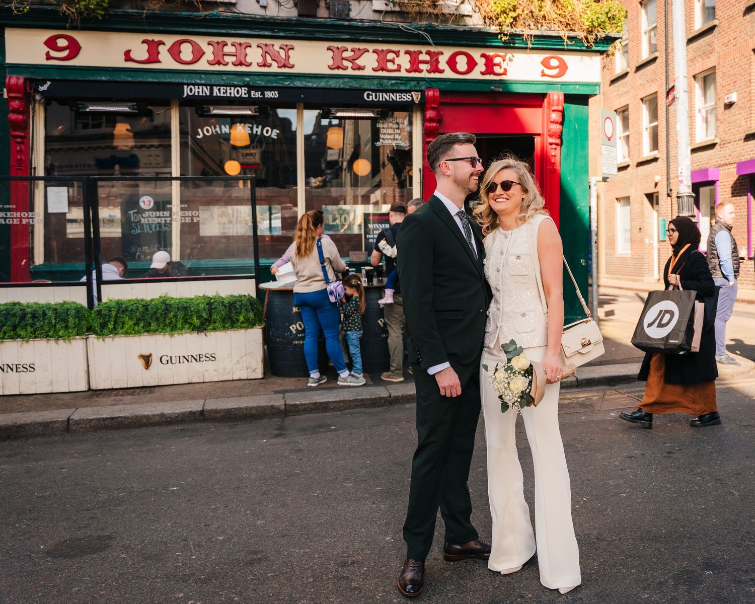 Wedding party walking along a Dublin street with colorful shop signs visible on a sunny autumn day. City Hall Dublin wedding photogrAPher