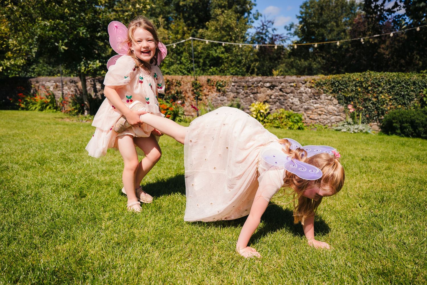 Playful outdoor moment in a garden with pink dresses and joyful expressions. . Village Barn Tyrrellspass wedding photographer Ireland