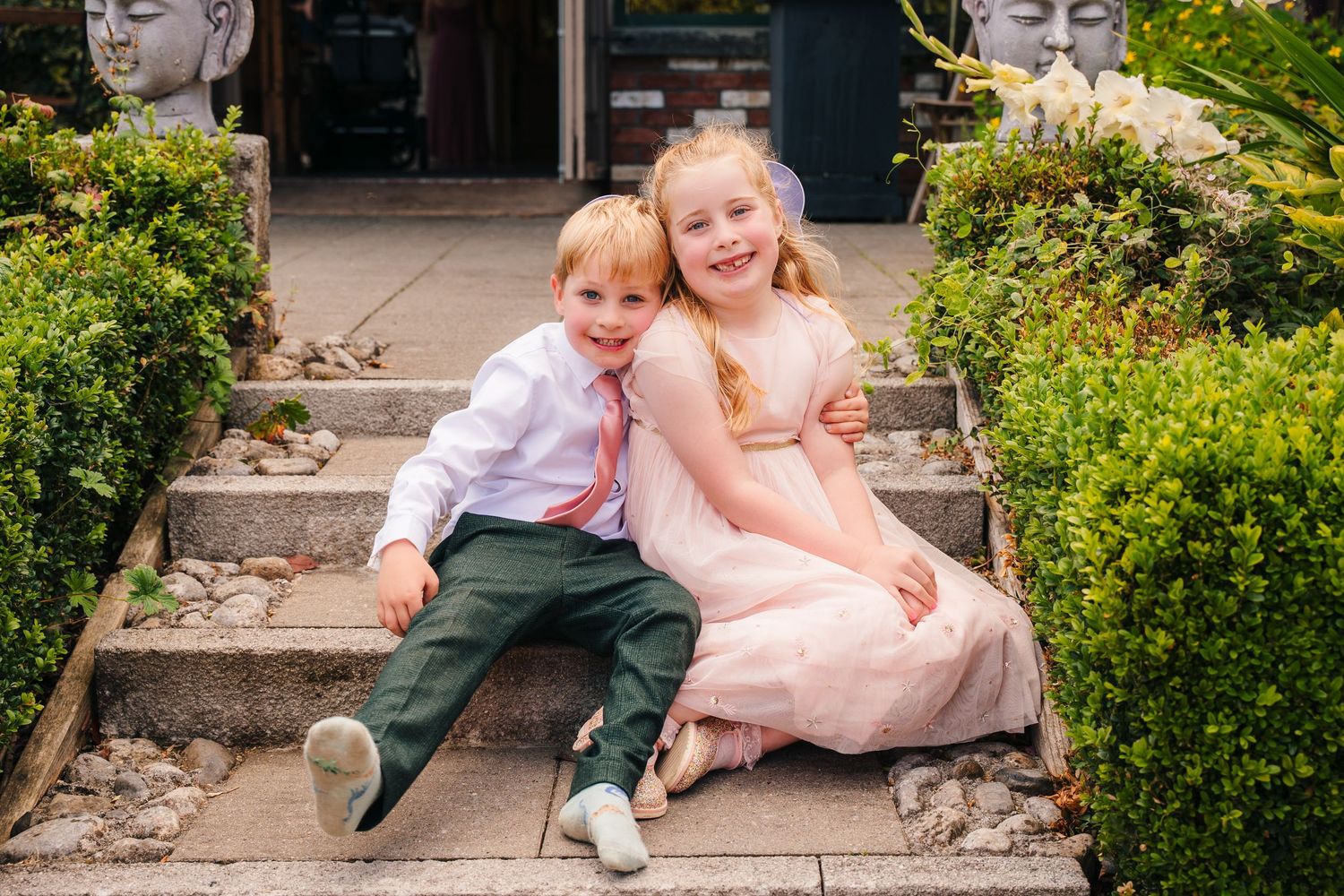 Two children in formal wear sit together on garden steps during a special occasion. . Village Barn Tyrrellspass wedding photographer Ireland