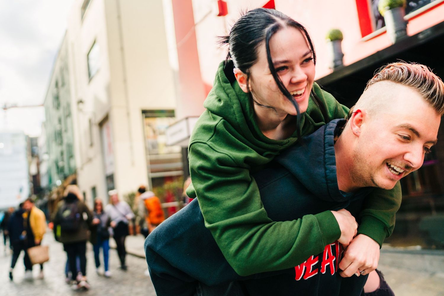 People laughing and embracing against a red urban backdrop with bright signage. PHOTOGRAPHER Dublin Ireland