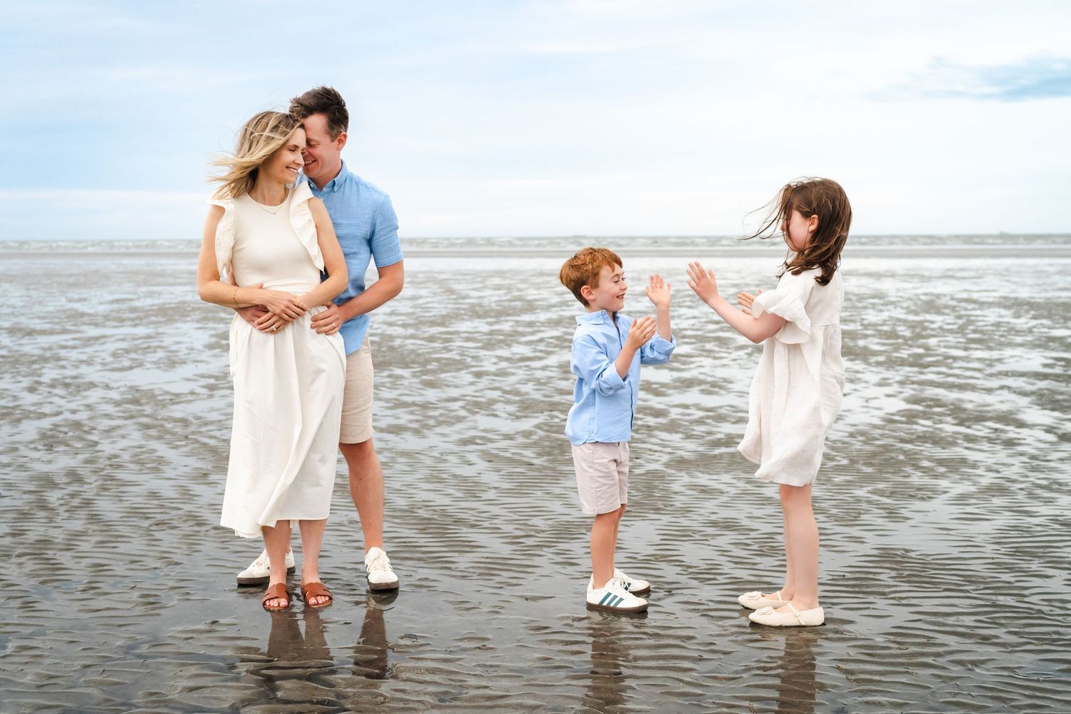 A family shares joyful moments together while playing at the edge of the ocean on a sandy beach.  Family photographer Dublin Ireland