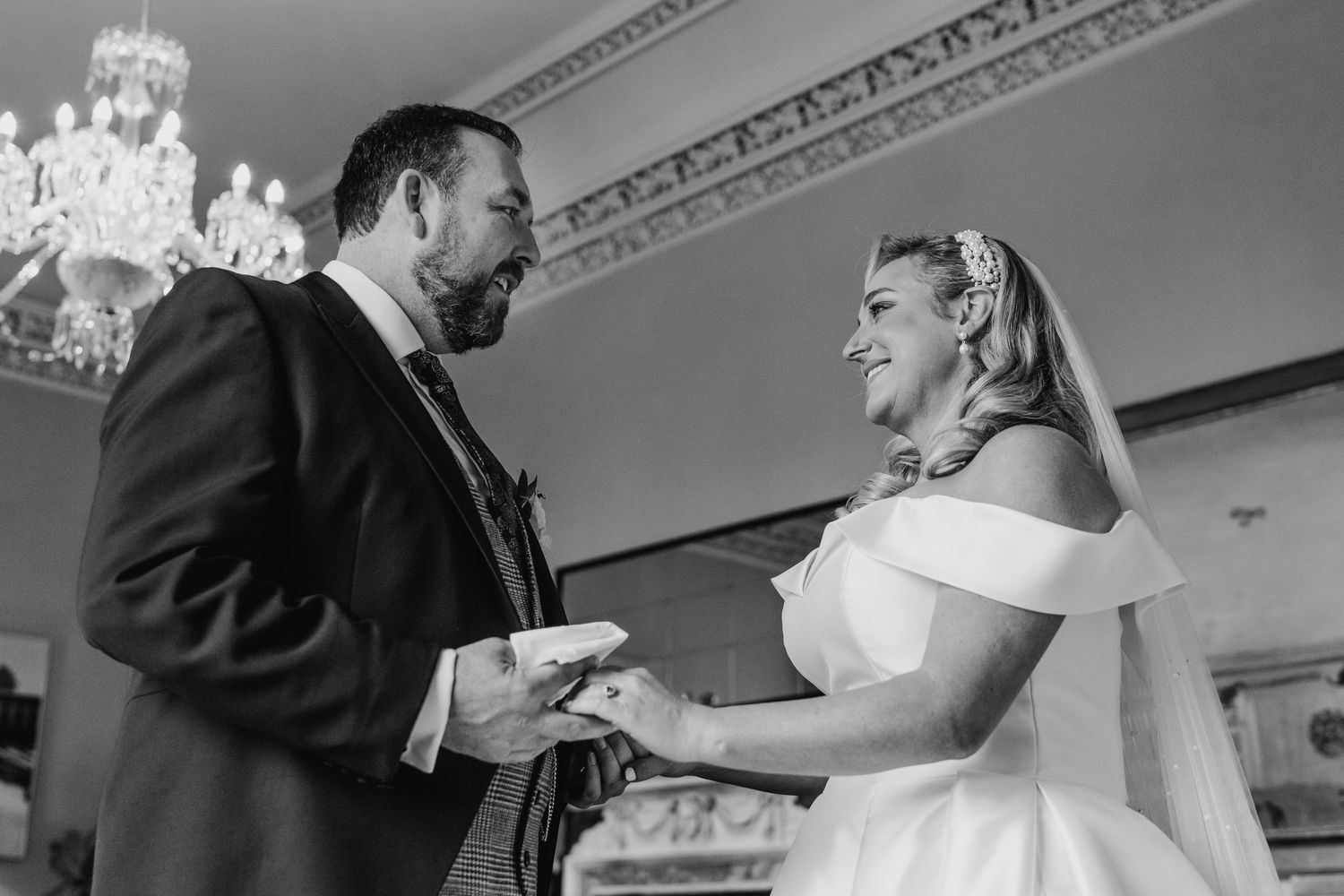 A couple shares a joyful moment during their wedding ceremony under an ornate chandelier. Virginia Park Lodge Wedding Photographer Cavan