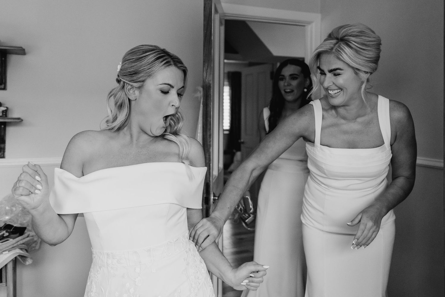 A black and white photo shows preparation in a room as two people in white dresses get ready for a special occasion. The Dean Dublin Wedding