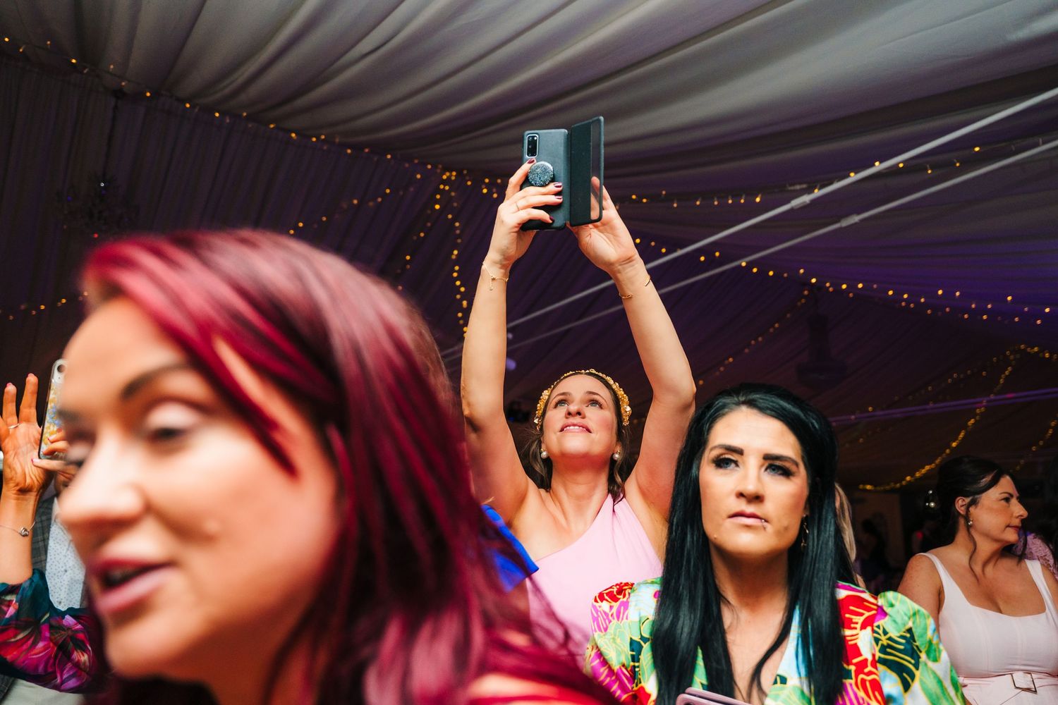 Wedding reception party guests dancing under decorative lights in a tent venue. LGBTQ Ashley Park Wedding Photographer