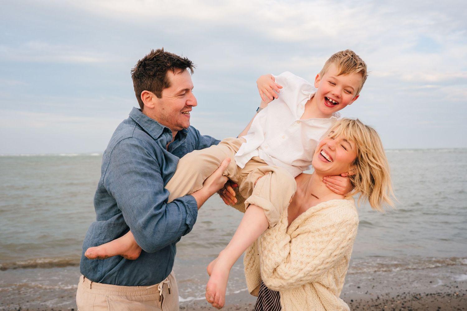 Happy family playing and laughing together at the beach with ocean and sky in the background. Family PHOTOGRAPHER Dublin