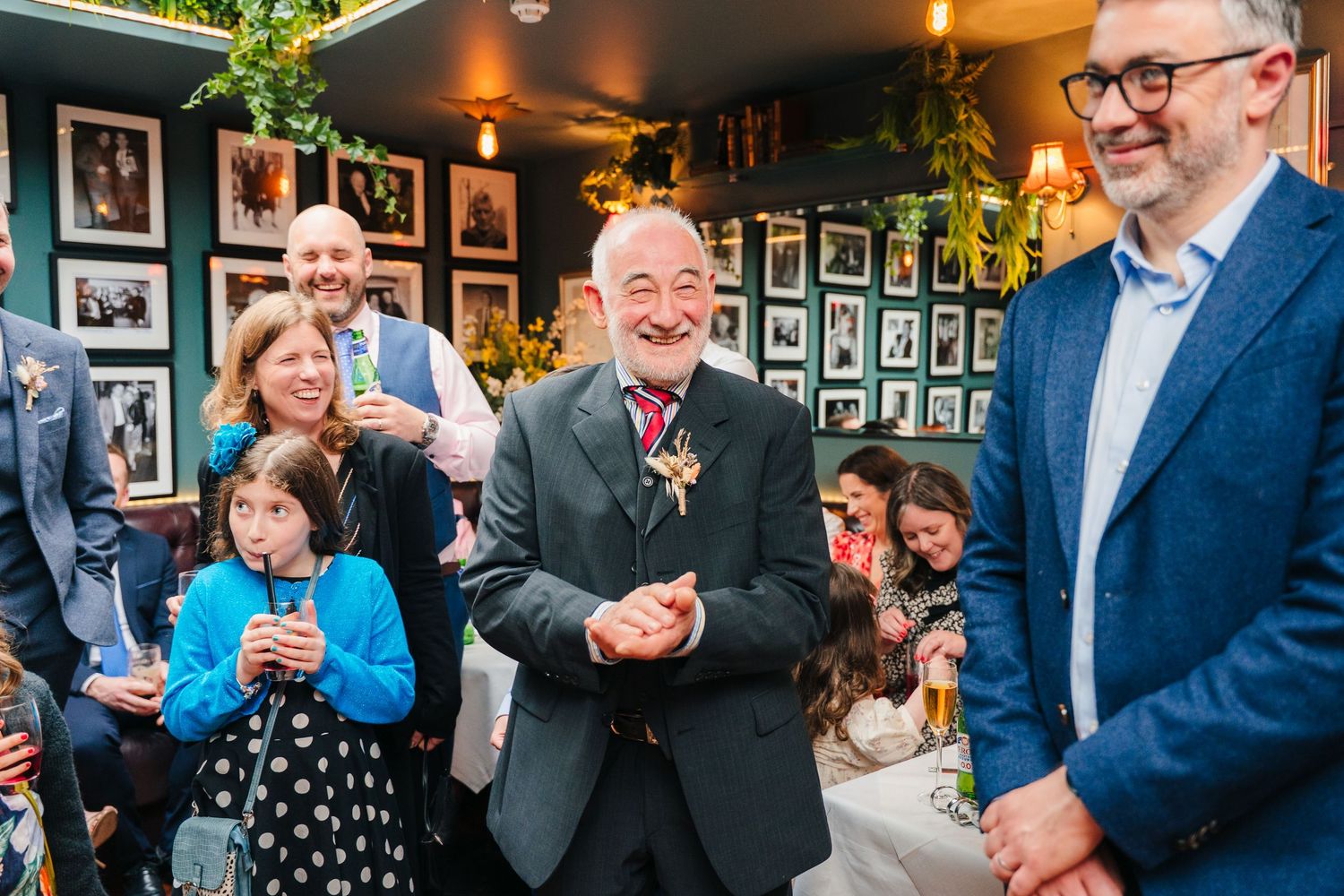 Wedding guests enjoying drinks and conversation in a dimly lit pub with photo-covered walls.