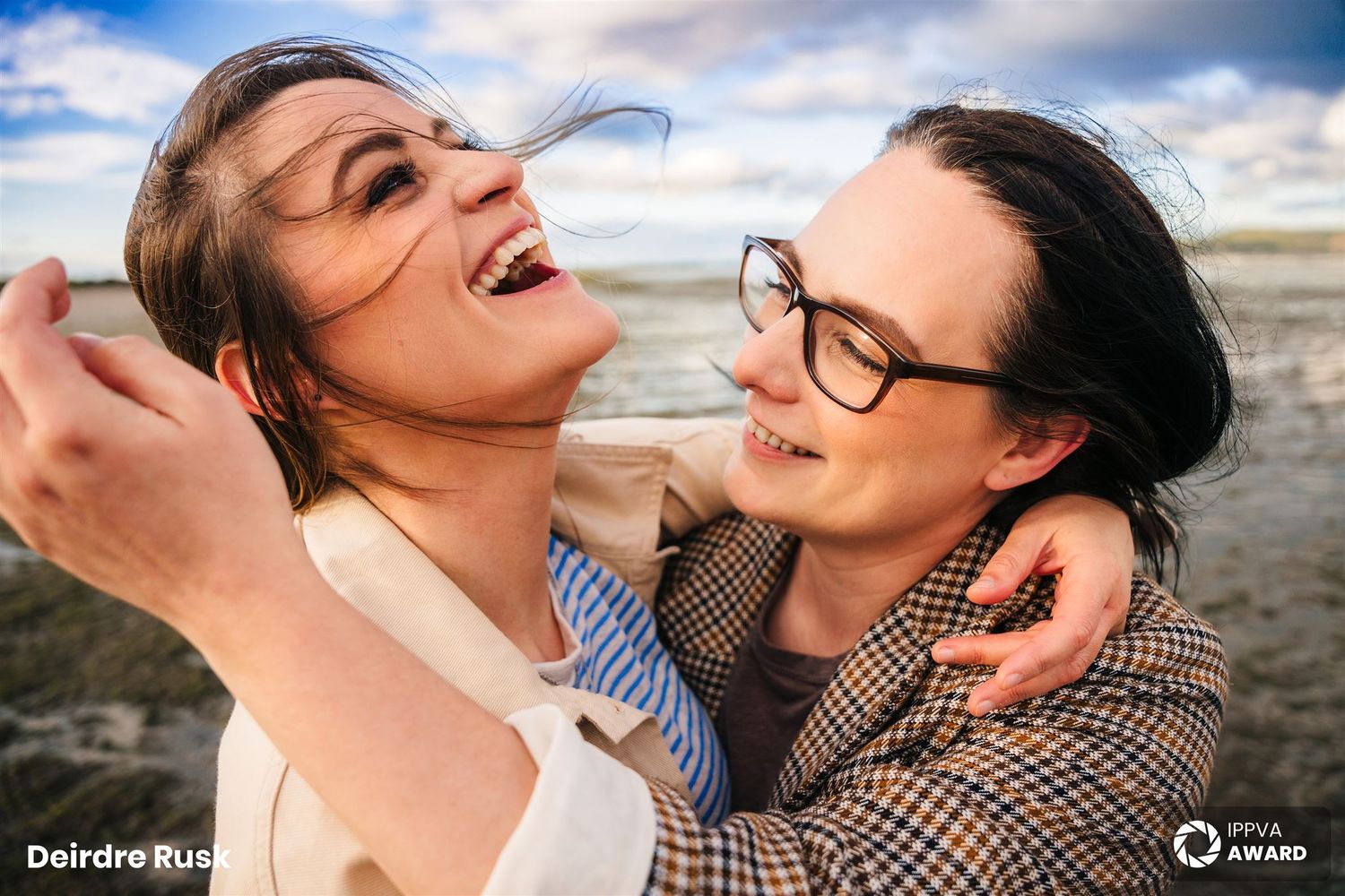 Two people laughing and embracing joyfully against a bright blue sky background. PHOTOGRAPHER Dublin