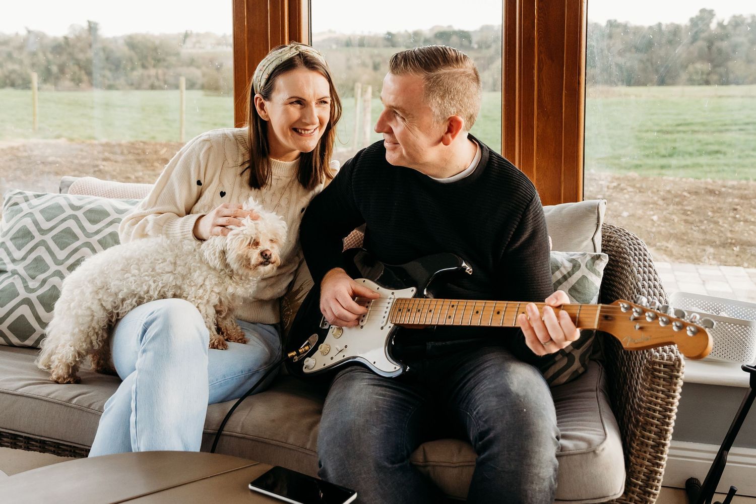 Happy couple relaxes on porch with dog while playing acoustic guitar on a beautiful autumn day. PHOTOGRAPHER Dublin