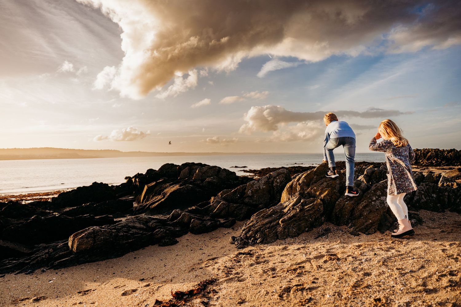 People climbing on rocky coastal cliffs at sunset with dramatic clouds and ocean views in the background. family PHOTOGRAPHER Dublin