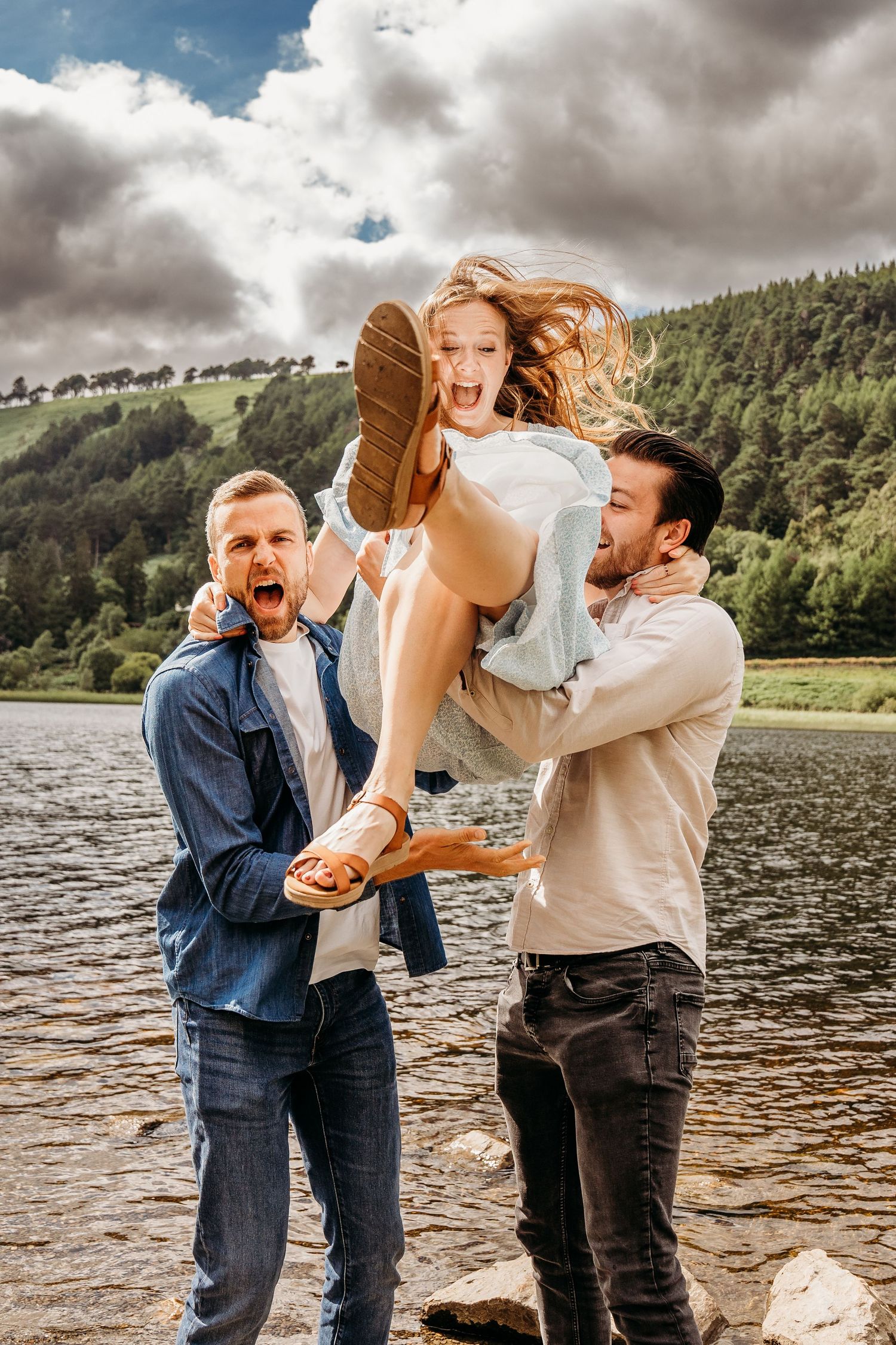Playful scene by a lake with people laughing and having fun on a cloudy day near mountains and forest. family PHOTOGRAPHER Dublin