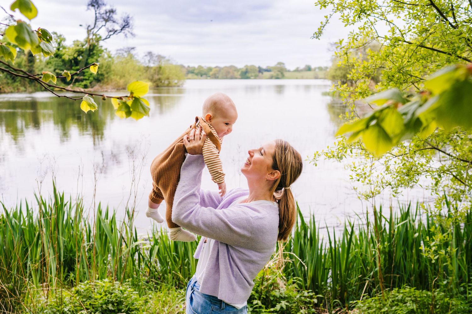 A joyful moment shared between two people by a serene lake surrounded by green foliage on a sunny day. Family PHOTOGRAPHER Dublin