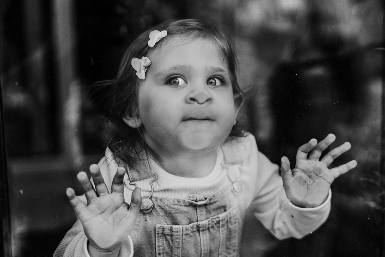 A young child in overalls raises both hands up with an excited expression in black and white. family PHOTOGRAPHER Dublin
