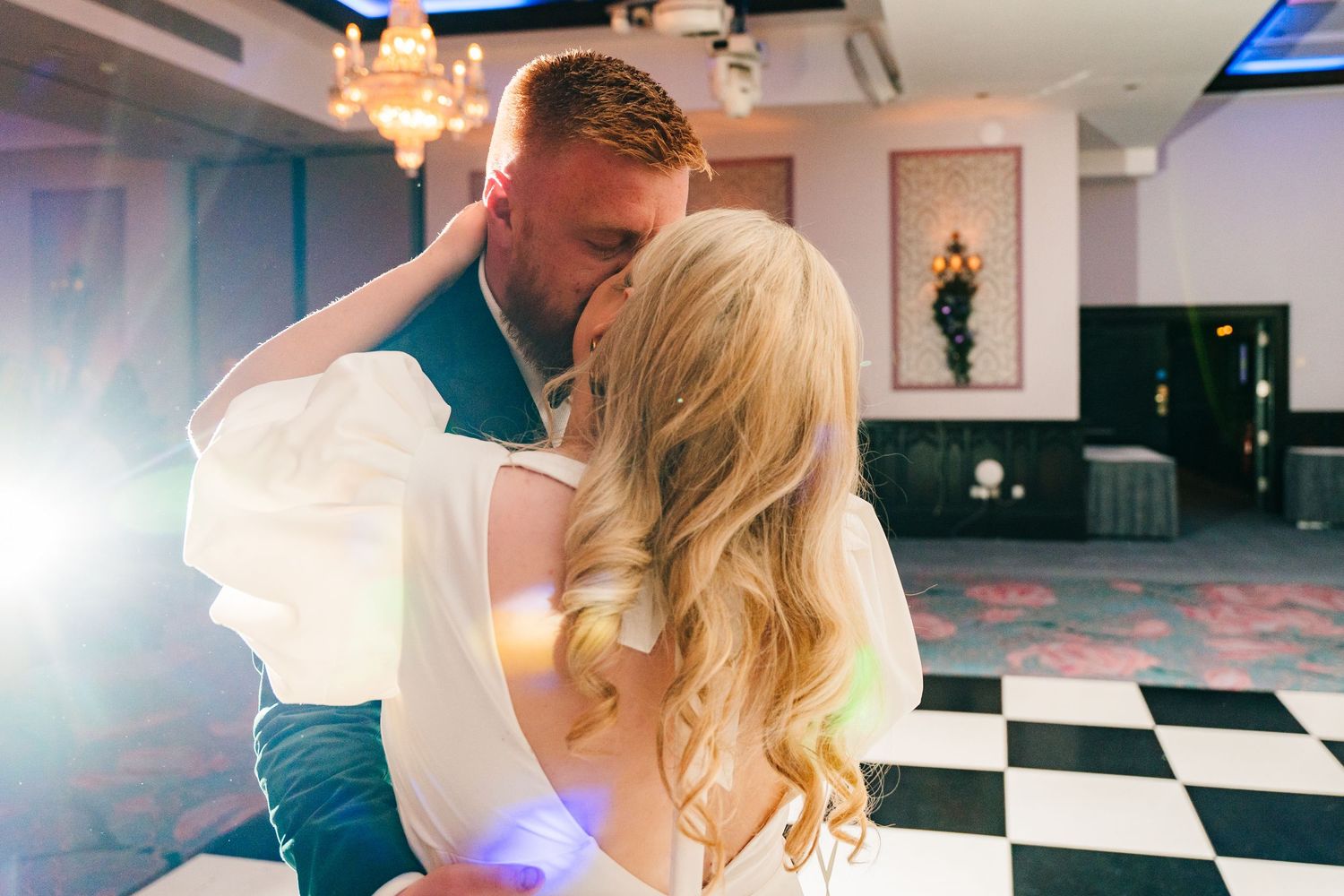 A couple shares their first dance at a wedding reception in a ballroom with black and white checkered floors. Wedding photographer dublin