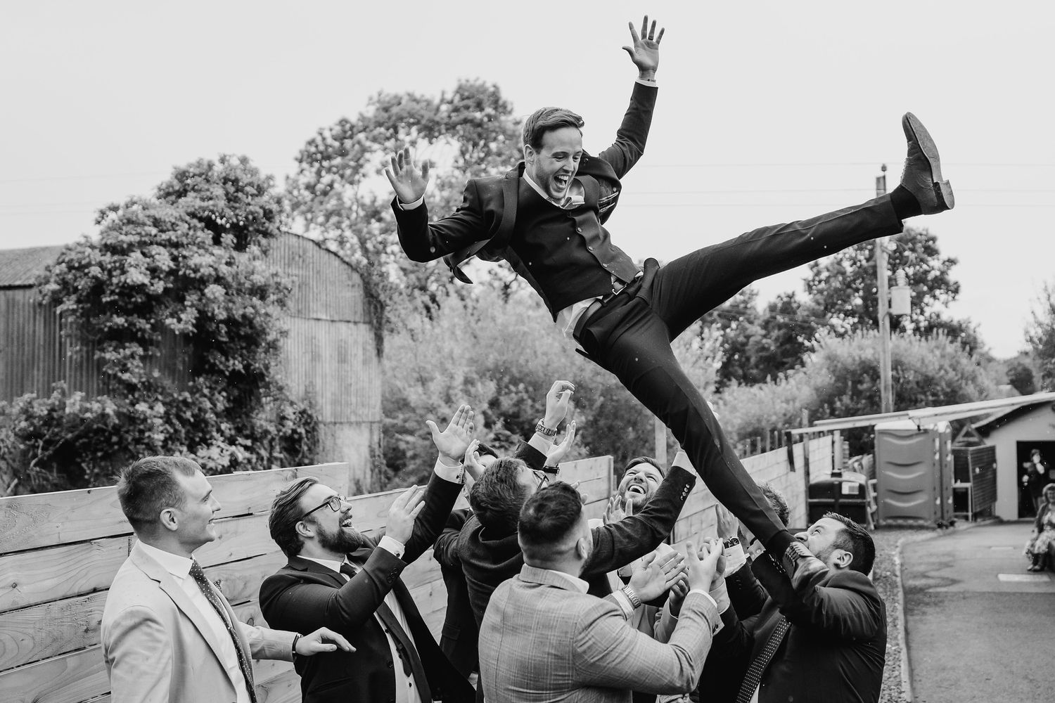 Dynamic black and white photo showing a person leaping high into the air as others lift them up in an energetic outdoor scene.