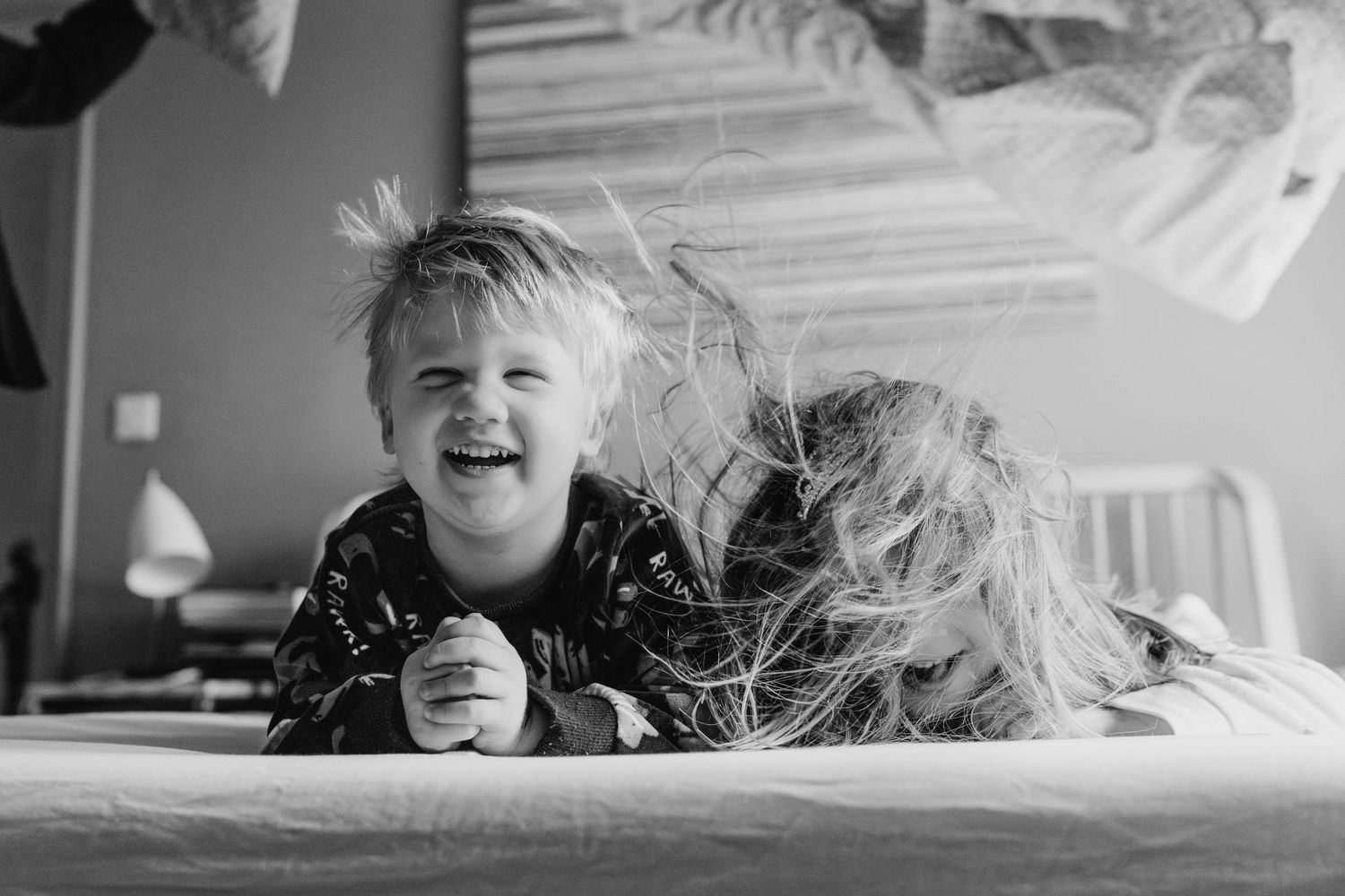A child laughs joyfully while lying on a bed in black and white photography. family PHOTOGRAPHER Dublin