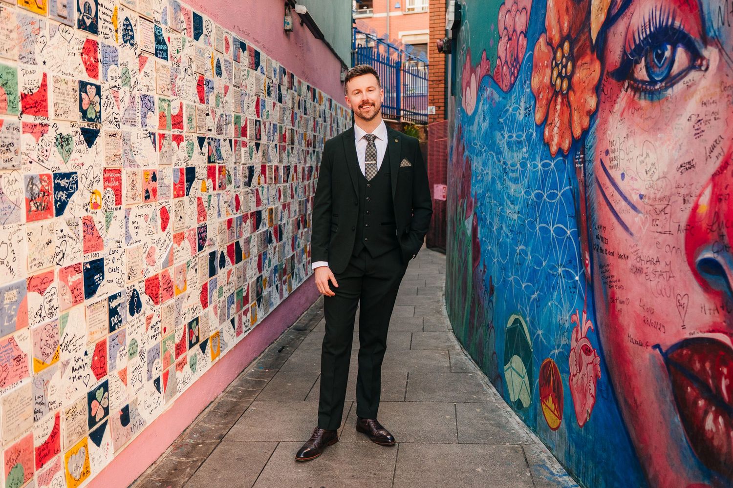 Couple poses in front of colorful graffiti wall filled with artistic posters and murals. City Hall Dublin wedding photogrAPher