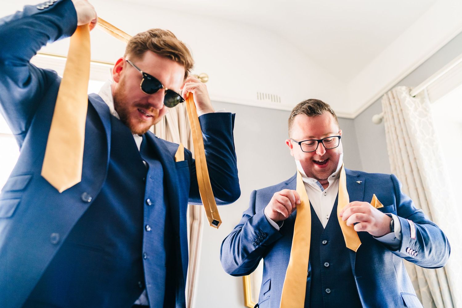 Poulaphouca Wedding photographer wicklow  Two groomsmen in navy suits and yellow ties help each other adjust their formal attire.
