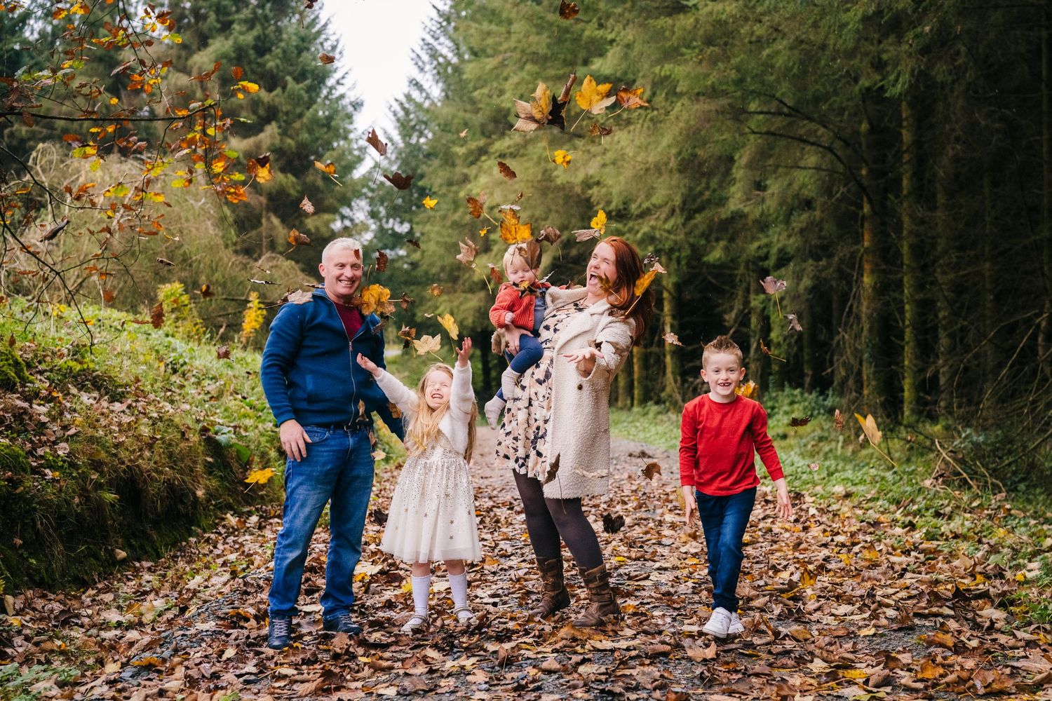 Family Photographer Dublin Ireland Several people stroll along a scenic forest trail covered in fallen autumn leaves.