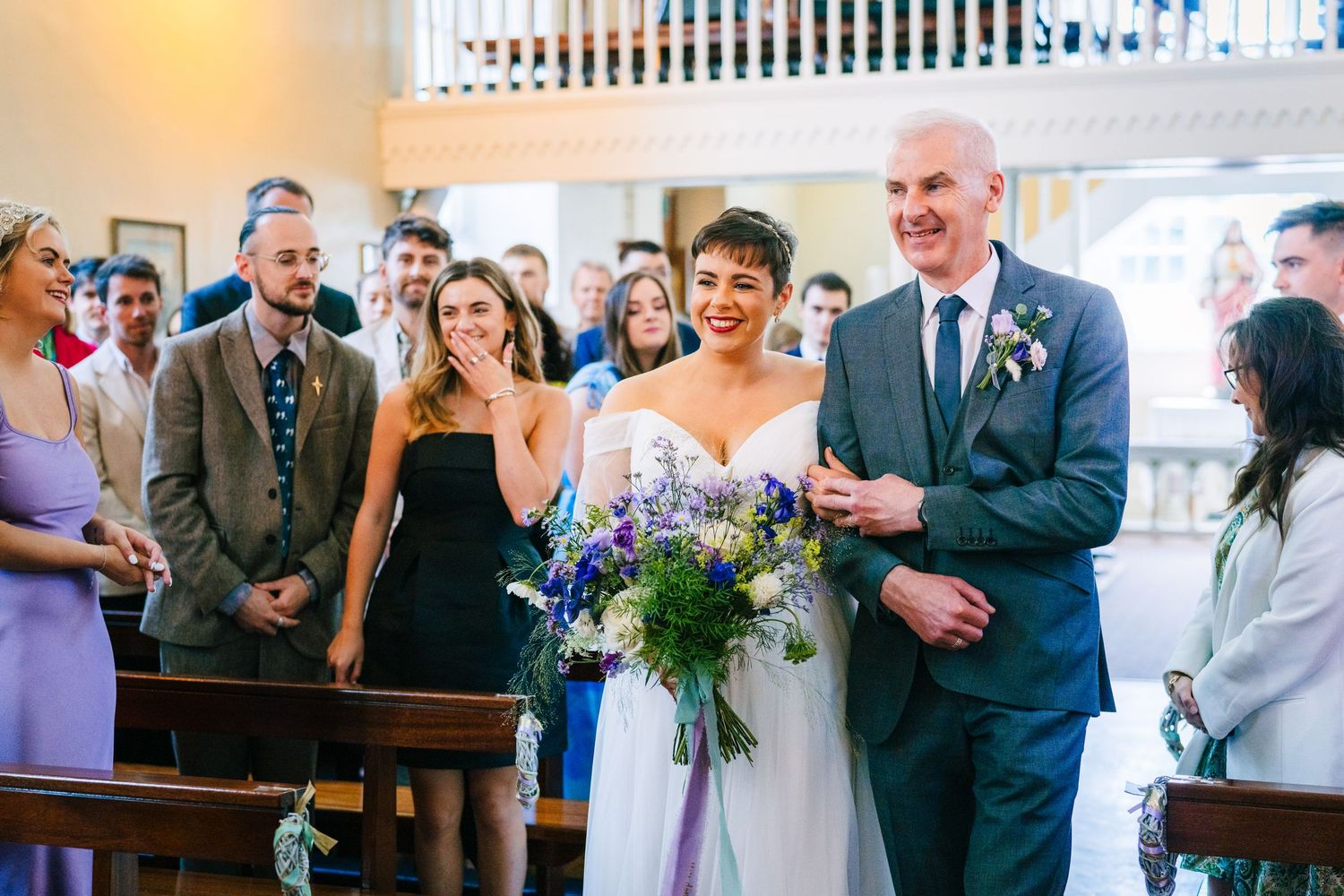 Wedding couple walks down church aisle with wedding party and guests looking on, surrounded by interior church decor.Millhouse slane wedding