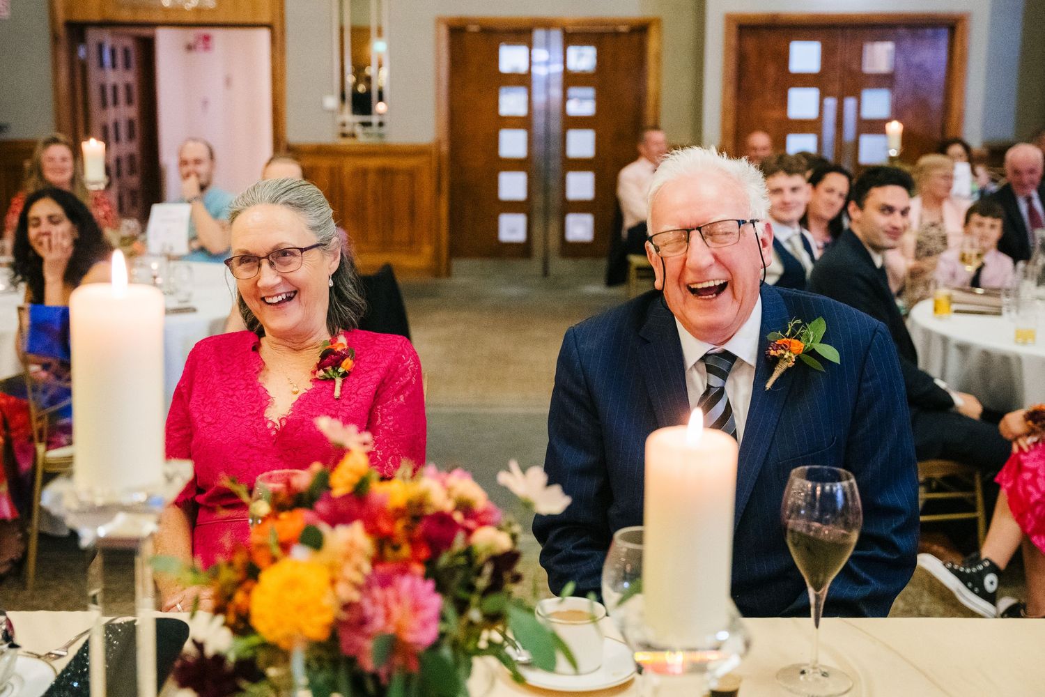 Wedding reception guests laugh joyfully at dinner table decorated with floral centerpieces and candles.Wedding Photography Trim Castle Irela