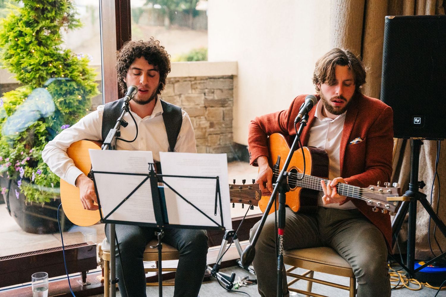 Musicians play acoustic guitars at an outdoor venue with a stone wall backdrop. Wedding Photography Trim Castle Ireland
