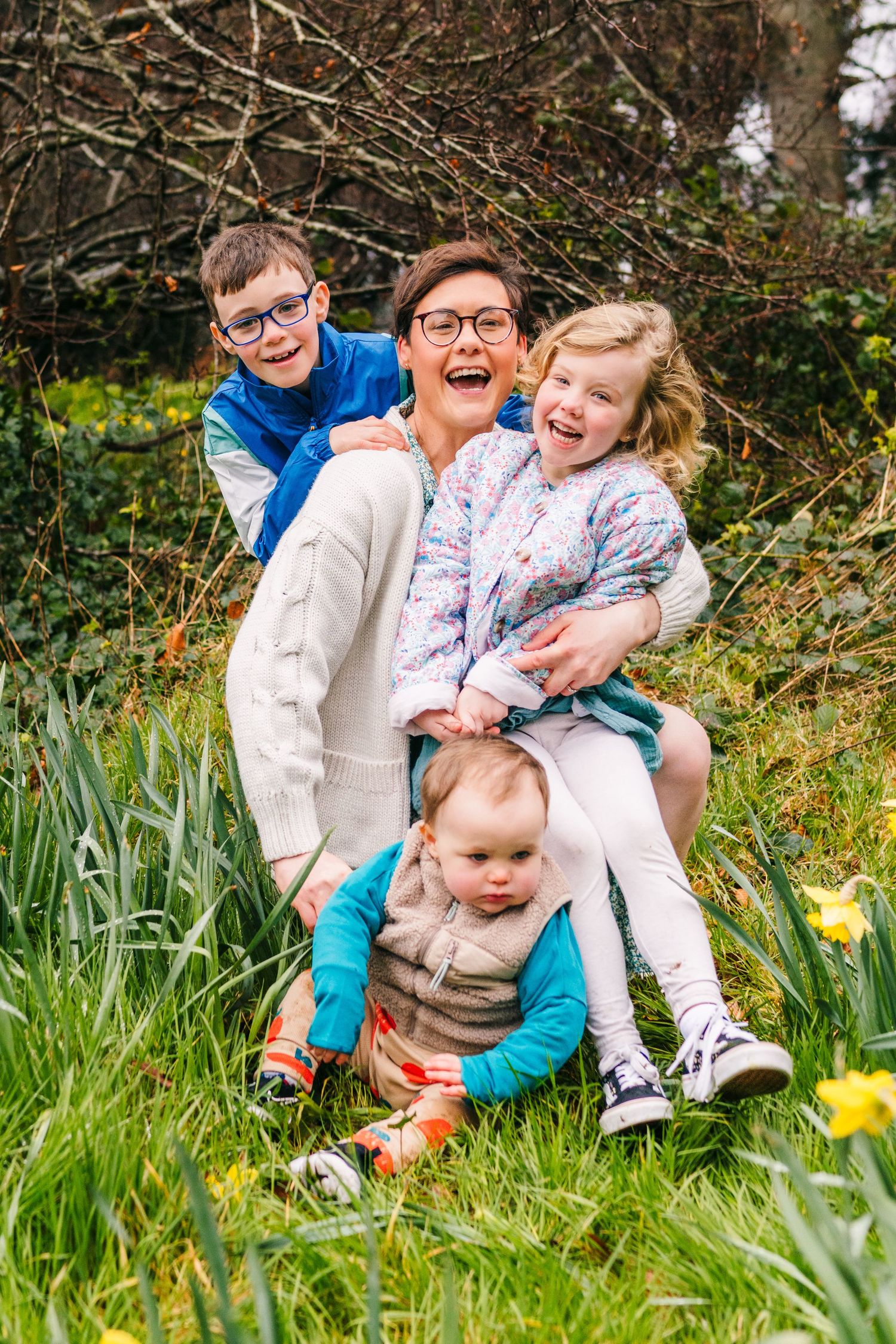 Family photographer Dublin Ireland  A joyful family enjoys a spring day together sitting in grass with yellow daffodils blooming nearby.