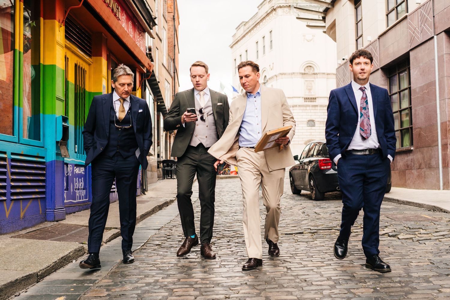 Four men in business attire walking down a colorful urban street together. PHOTOGRAPHER Dublin Ireland Wedding