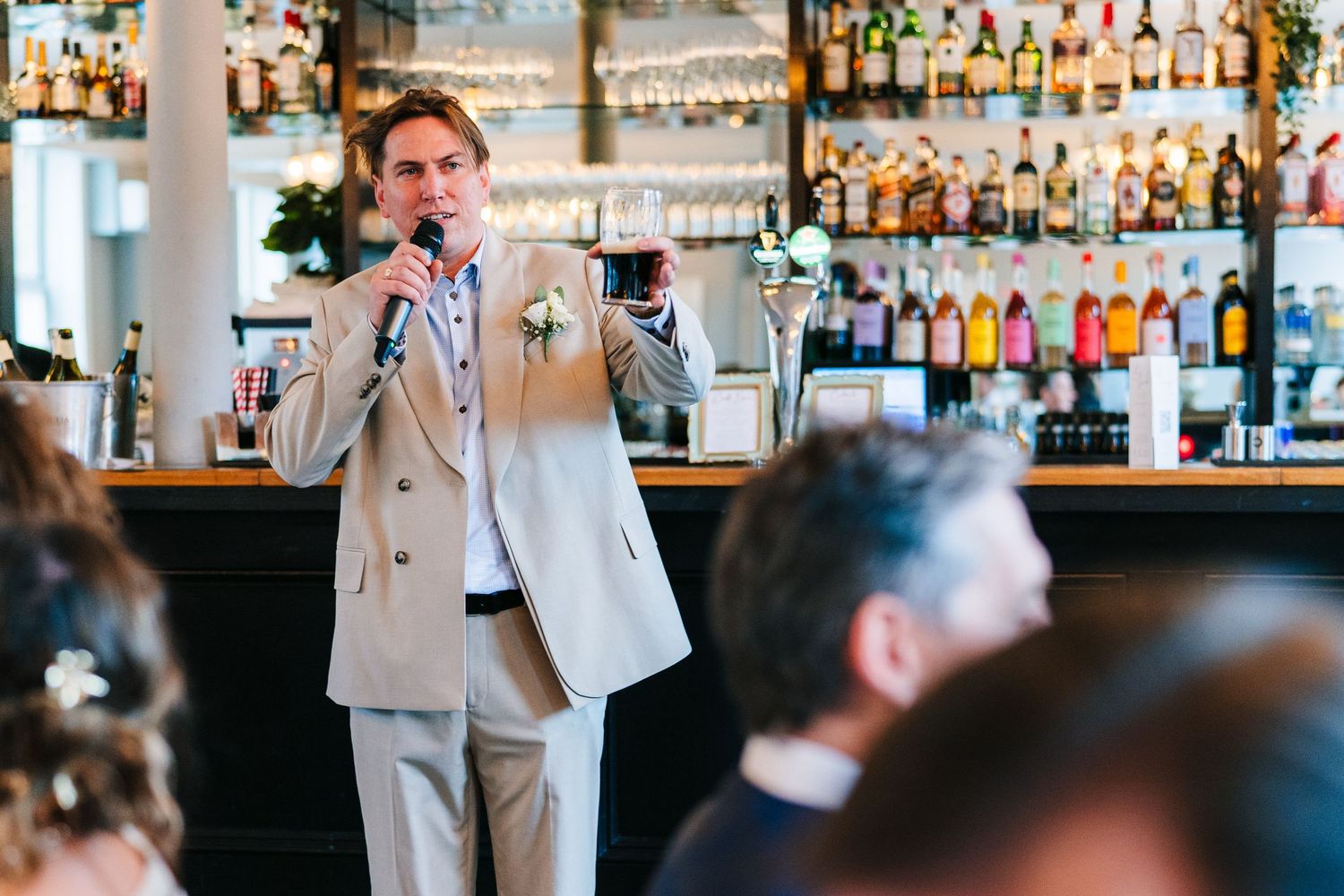 Person in light colored suit delivers speech at wedding reception bar area.PHOTOGRAPHER Dublin Ireland Wedding