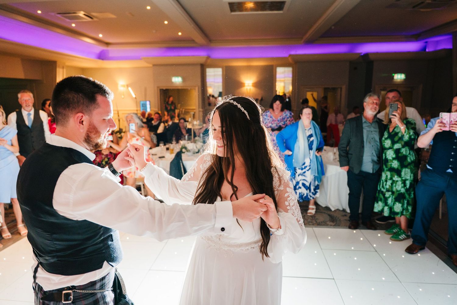 Guests dancing and celebrating at a wedding reception with purple lighting effects. Portmarnock Hotel Wedding PHOTOGRAPHER Dublin